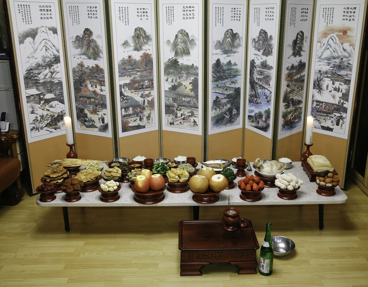 A real charye table set for an ancestral rite, with rice cakes, fruit, fish and candles in front of a painted folding screen